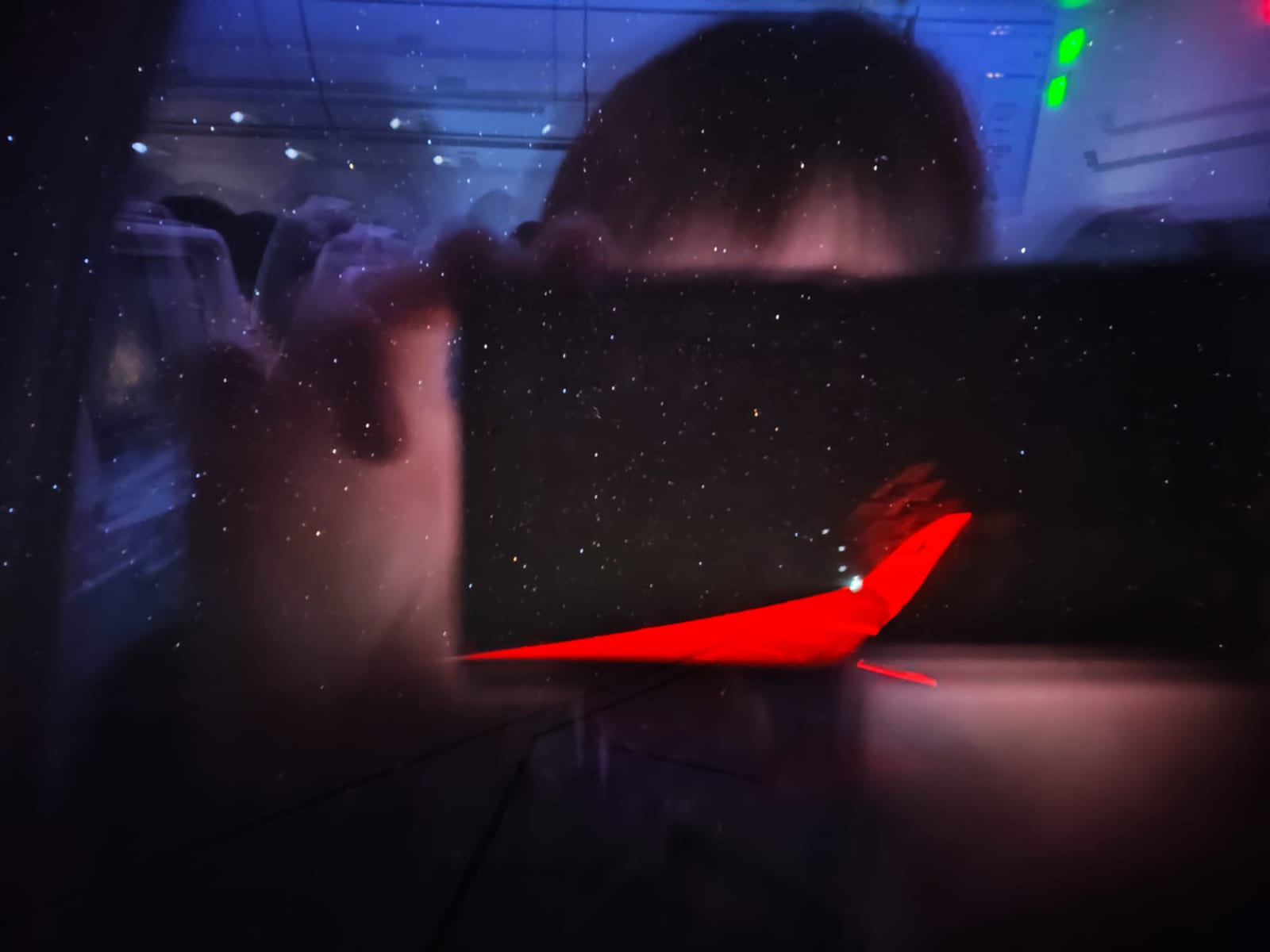 夜の窓越しにスマートフォンで撮られた、赤い尾翼をもつ飛行機の記録